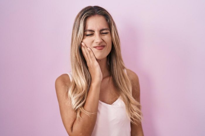 young blonde woman standing pink background touching mouth with hand with painful expression because.jpeg