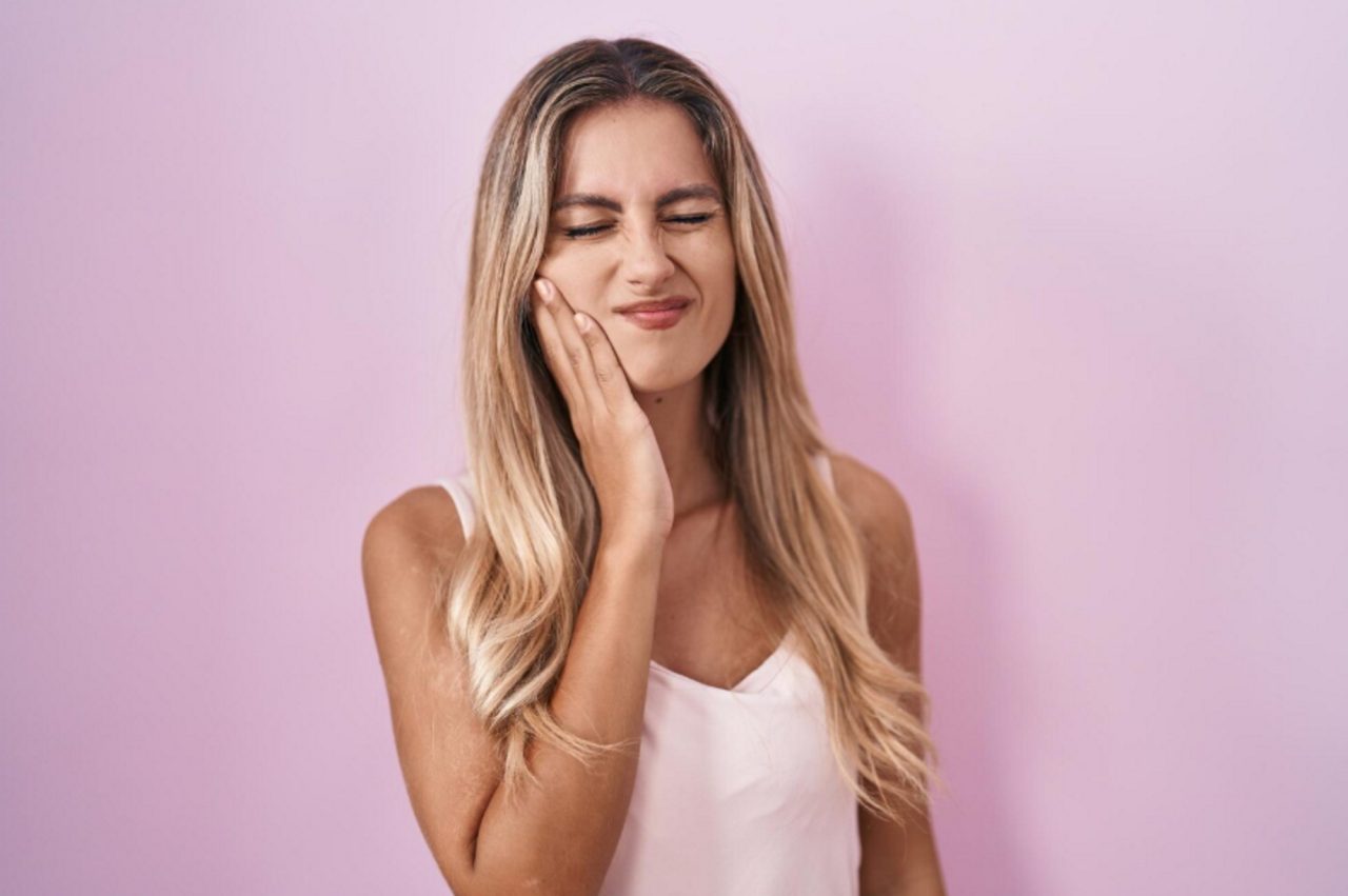 young blonde woman standing pink background touching mouth with hand with painful expression because.jpeg